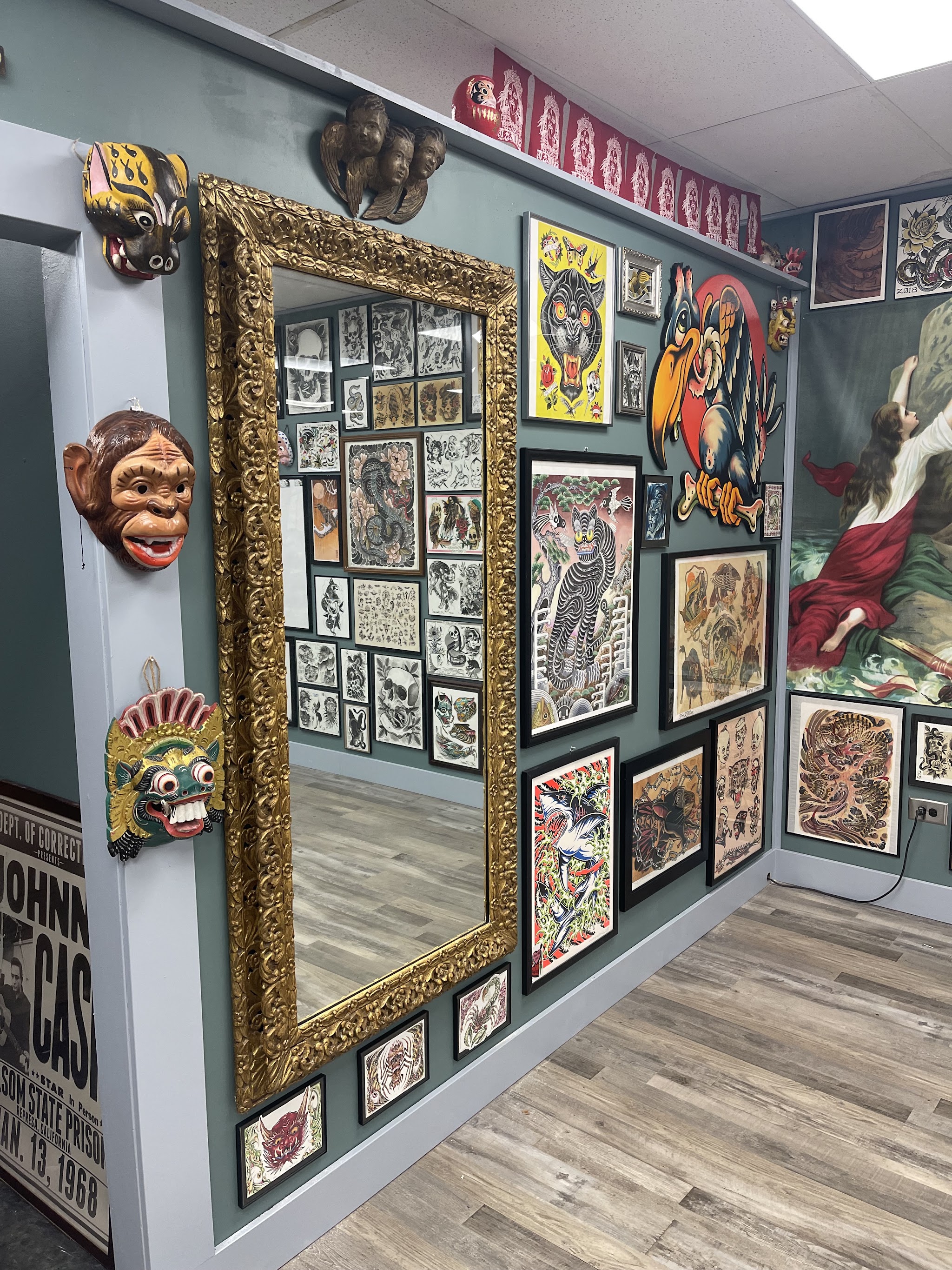 Inside Setting Sun Tattoo: framed flash art covering a sage green wall beside a large ornate gilt mirror